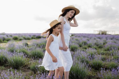 woman and kid in straw hats holding hands while walking in lavender meadow