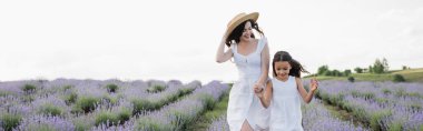 excited woman and girl in white dresses holding hands and running in field, banner