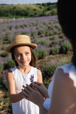 smiling girl in straw hat giving lavender flowers to blurred mom