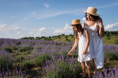 woman and child in straw hats walking in field near blooming lavender