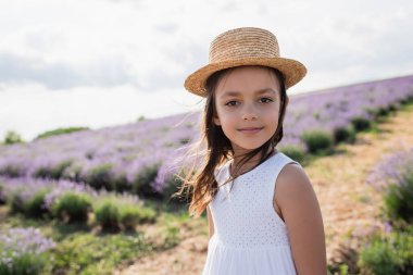 smiling girl in sun hat and white dress looking at camera in blurred lavender field