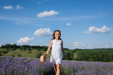 happy girl in summer dress walking in lavender field under blue sky with white clouds