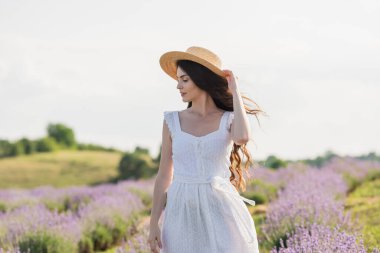 woman in straw hat and white dress standing in blurred lavender field