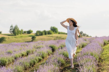 full length of woman in straw hat and white dress walking in lavender field