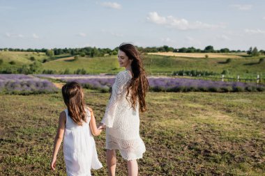 smiling pregnant woman in openwork dress walking with daughter in countryside