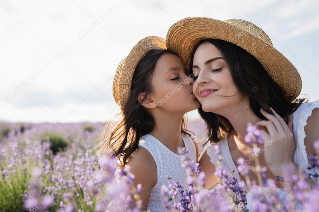 child kissing woman smiling with closed eyes in flowering field