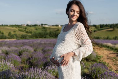 happy pregnant woman in white dress in summer lavender field