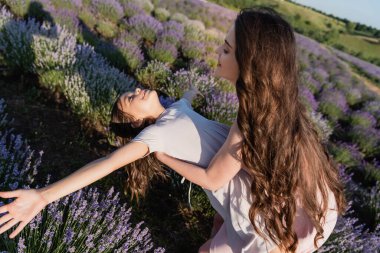 brunette woman with long hair playing with happy daughter in lavender field