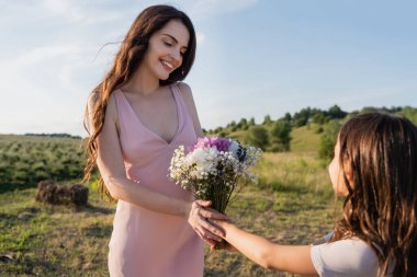 girl presenting flowers to happy mother in meadow on summer day