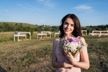 pleased woman with flowers smiling at camera on farmland clipart