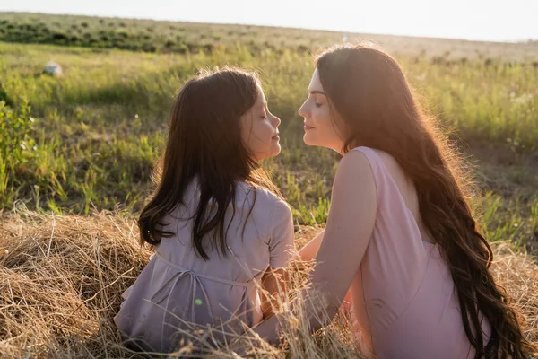 mother and child sitting face to face with closed eyes on hay in field