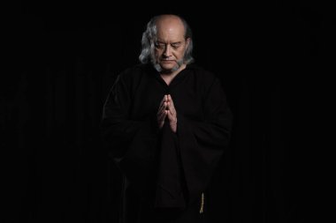 Gözleri kapalı ve dua eden siyah elleri olan kıdemli keşişin önü.