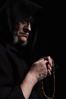 medieval monk in hood holding rosary isolated on black clipart