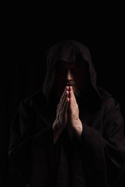 Siyah kapüşonlu cüppeli keşişin siyah üzerine izole edilmiş dua edişi.