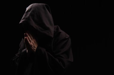 mysterious priest in hooded robe praying isolated on black clipart