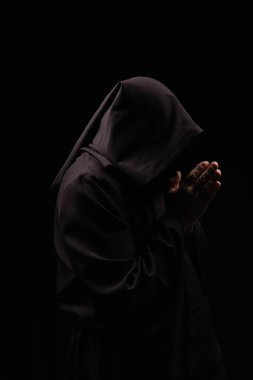 Kapüşonlu gizemli keşişin siyah üzerinde yalnız dua edişinin yan görüntüsü