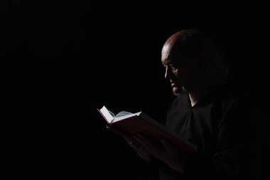 Cüppeli gizemli keşiş karanlıkta incili okuyor.