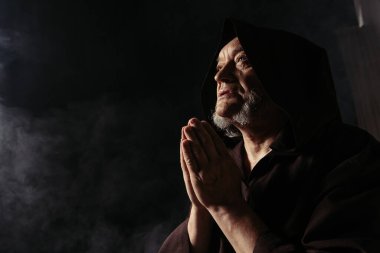 Siyah başlıklı keşişin karanlık arka planda dua edişinin alçak açılı görüntüsü
