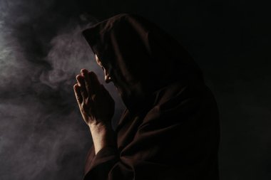 Kapüşonlu papazın yüzü siyaha boyanmış dumanla dua ederken.