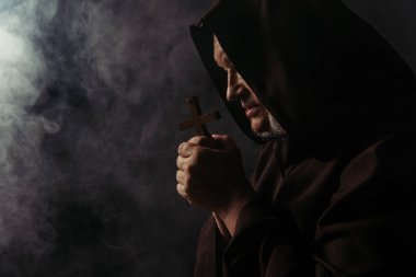 Üzerinde kutsal haç olan keşişin dumanla siyah üzerine dua edişinin yan görüntüsü.