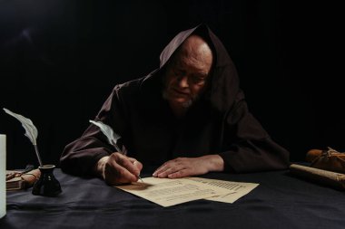medieval abbot writing chronicle on parchment near inkpot isolated on black clipart