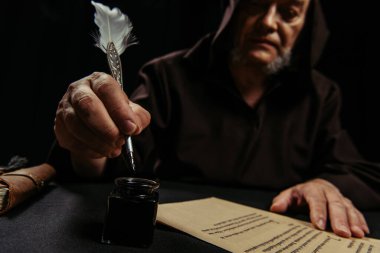 Bulanık keşiş elinde tüy kalemi, mürekkep kabının yanında ve siyah üzerine izole edilmiş antik el yazması.