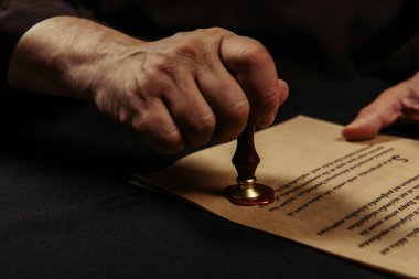 cropped view of monk stamping chronicle with wax seal isolated on black clipart