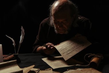 Ortaçağ el yazmalarındaki balmumu mührüne bakan gizemli keşiş siyah üzerine izole edilmiş.