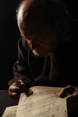 Ortaçağ rahibi, siyah üzerine izole edilmiş antik el yazmasının balmumu mührüne bakıyor.