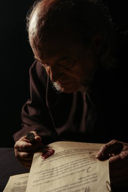 medieval priest looking at wax seal on ancient manuscript isolated on black clipart