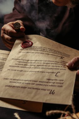 Keşişin parşömen tutarken kısmi görünümü koyu arkaplan üzerinde el yazması ve balmumu mühür ile