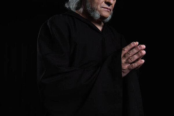 cropped view of bearded monk in cassock praying isolated on black