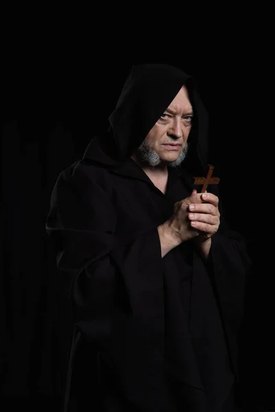 stock image medieval monk in hooded robe holding crucifix and looking at camera isolated on black