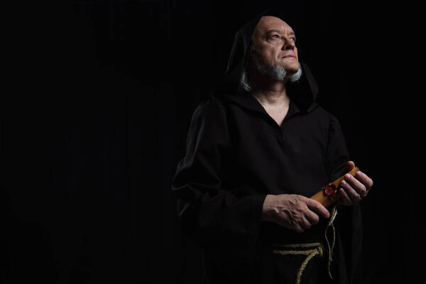 senior monk with rolled manuscript looking away isolated on black
