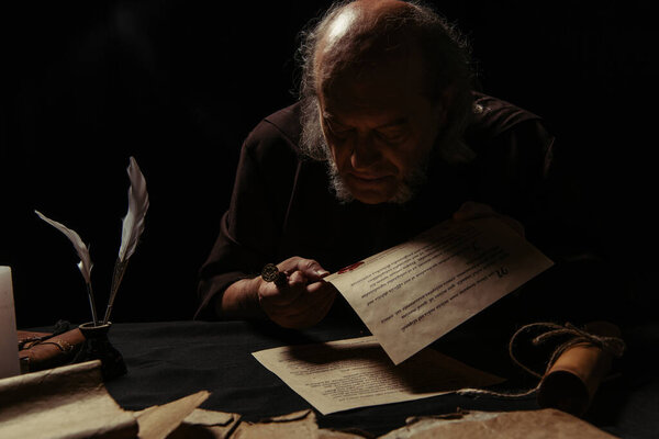 mysterious monk looking at wax seal on medieval manuscript isolated on black