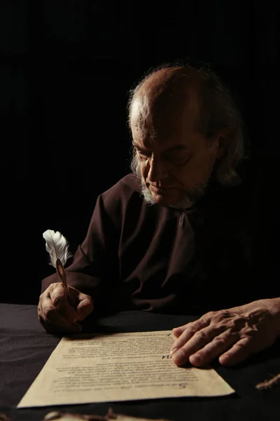 mysterious monk writing chronicle with quill pen in darkness isolated on black