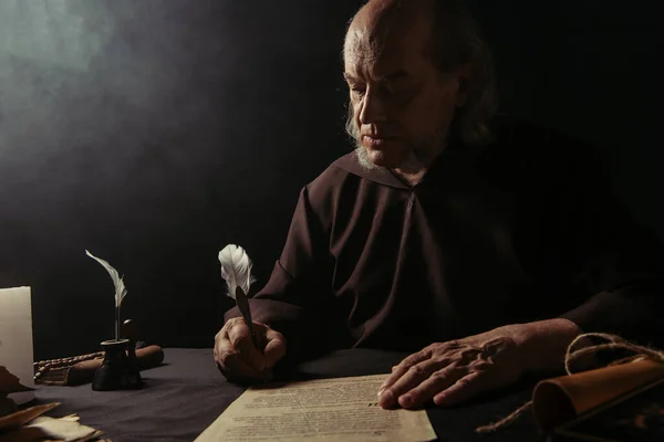 medieval priest in black robe writing manuscript on dark background