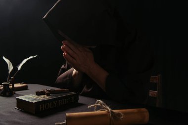 Papaz yüzünü gizliyor, dua eden elleri haçın yanında, kutsal İncil 'in üstünde, siyahların üzerinde.