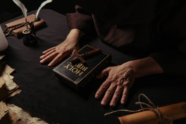 İncil ve ortaçağ parşömenlerinin yakınındaki keşişin siyah masa üzerindeki kısmi görüntüsü