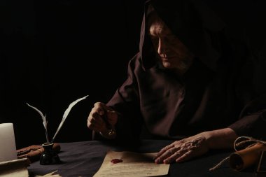Siyah üzerine balmumu mühür yapıştırılmış kapüşonlu cüppeli başrahip.