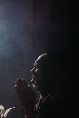 Başlıklı keşişin siyah arka planda fotokopi aletiyle dua edişinin yan görüntüsü