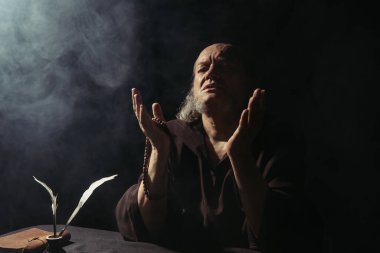 Ortaçağ başrahibi müsveddelerin yanında dua ediyor ve tüy kalemleriyle siyah üzerine tüy döküyor.
