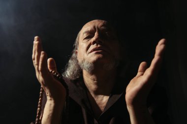 Siyah arka planda kapalı gözlerle dua eden kıdemli başrahibin önünde.