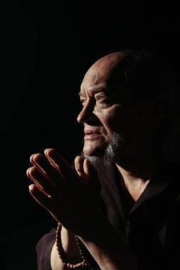 Yaşlı sakallı rahip kara dualar ederken gözlerini kaçırıyor.