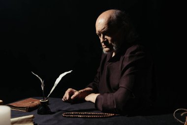 Düşünceli keşiş gece mürekkep küpü ve tespih yanında siyahların üzerinde yalnız başına oturuyor.