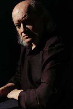 Katı ve düşünceli bir rahip siyah kameraya bakıyor.