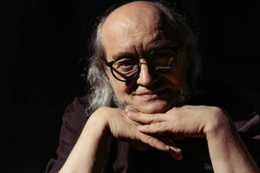 pozitif ortaçağ filozofu. Gözlüklü. Çenesinin yanında el ele tutuşuyor ve kameraya gülümsüyor.