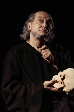 medieval religious philosopher with skull looking up while thinking isolated on black clipart