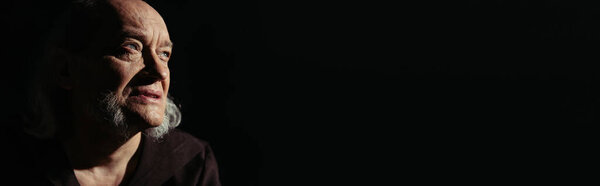 portrait of pensive and serious priest looking away isolated on black, banner