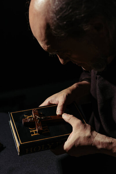 средневековый монах, держащий святой крест и Библию в темноте, изолированной на черном